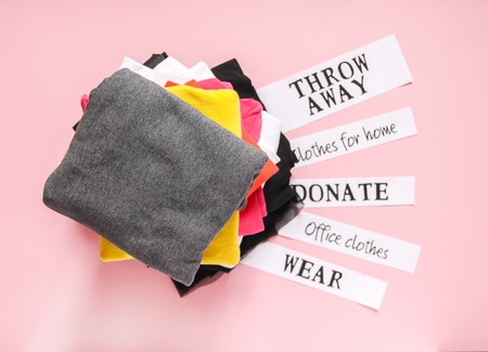 Clothes sorting in wardrobe for donation, wearing at office and home and discard with paper notes on soft pink background.の写真素材