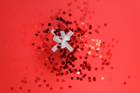 Small red gift box with silver ribbon on bright background with decorative small heart tinsel.の写真素材