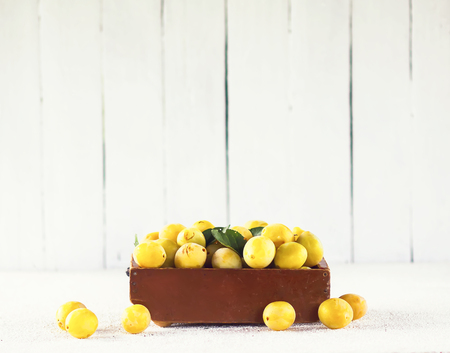 Fresh yellow plums. Ripe fruits in a wooden box on white boards backgroundの写真素材