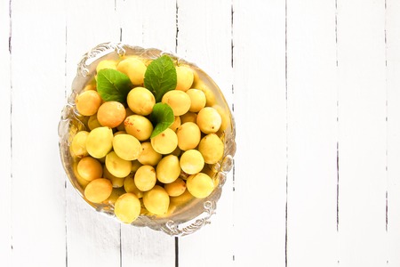 Fresh yellow plums. Ripe fruits in a plate on white boards backgroundの写真素材