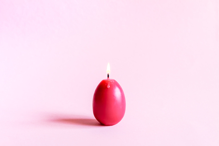 Traditional Easter decor. Group of bright burning paraffin candles in the shape of colorful eggs on soft pink background.の写真素材