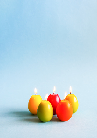 Traditional Easter decor. Bright burning paraffin candles in the shape of colorful eggs on blue background.の写真素材