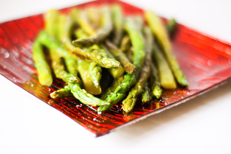 Green grilled asparagus on a red square glass plateの写真素材