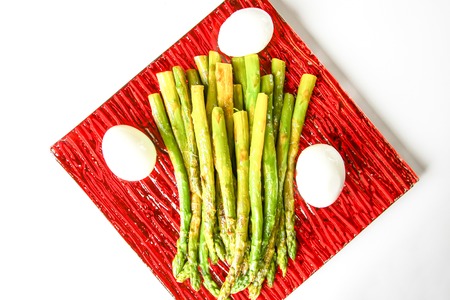Green grilled asparagus and baked eggs on a red square glass plateの写真素材