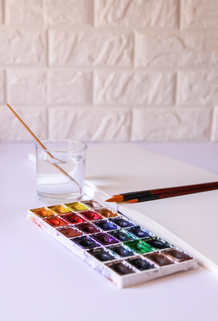 Watercolor paints, water in glass, brushes and paper on white background. Painting tools. Flat lay, top viewの写真素材