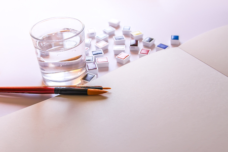 Watercolor paints, water in glass, brushes and paper on white background. Painting tools. Flat lay, top viewの写真素材