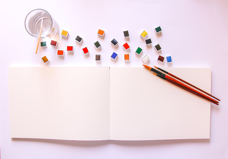 Watercolor paints, water in glass, brushes and paper on white background. Painting tools. Flat lay, top viewの写真素材
