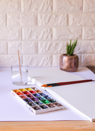 Watercolor paints, water in glass, brushes and paper on white background. Painting tools. Flat lay, top viewの写真素材