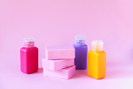 Bright plastic small travel bottles for liquids and bars of soap on a soft pink background. Accessories set for body care and hygiene.の写真素材