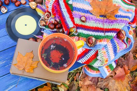 Autumn composition of yellow ceramic cup of herbal tea and vintage vinyl records on aged wooden background with bright handmade crocheted plaid, old book, fall autumn leaves and chestnutsの写真素材