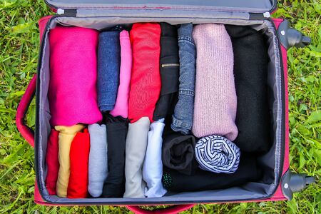 Open suitcase on the green grass with different clothes folded vertically. Vertical storage for easy and compact space saving in travel packの写真素材