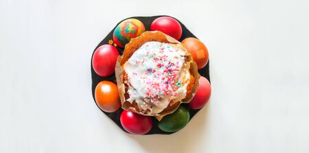 Sweet Easter cake and bright colorful eggs on white table surface.