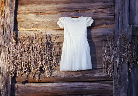 Linen dress hanging on a hanger outdoors on wooden rough wall backgroundの写真素材