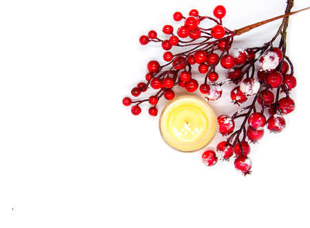 Festive Christmas or New Year composition with red holly berries in snow and burning wax candle on white backgroundの写真素材