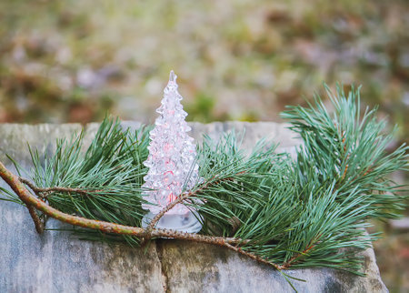 Glass toy luminous Christmas tree outdoors with pine branch on wooden surface. Festive decorating.