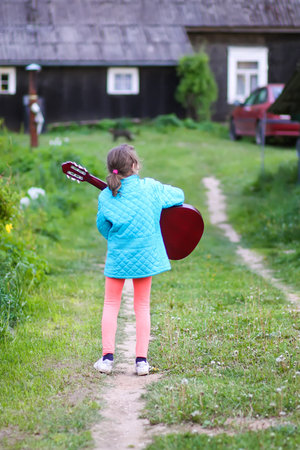 Little girl playing guitar and singing outdoors on green meadow at spring. Happy child on rural yard.の写真素材