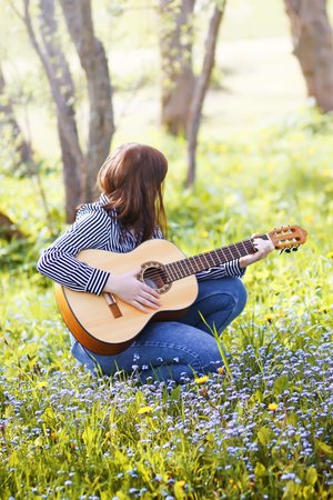 Blonde atrtractive teenager girl playing guitar in spring garden