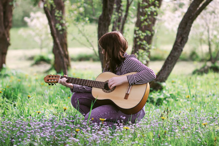 Blonde atrtractive teenager girl playing guitar in spring garden.の写真素材