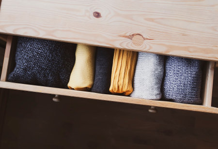 Open wooden dresser drawer with warm knitted woolen clothes. Home vertical storage. Wardrobe organisation. Trendy colors.の写真素材