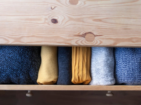 Open wooden dresser drawer with warm knitted woolen clothes. Home vertical storage. Wardrobe organisation. Trendy colors.の写真素材