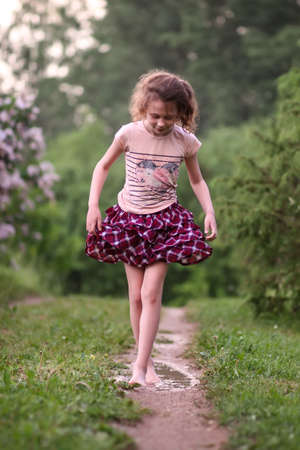 Barefoot happy little girl walks through a puddles of water after the summer rain in countryside.の写真素材