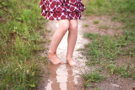 Barefoot girl walks through a puddles of water after the summer rain in countryside.の写真素材