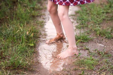 Barefoot girl walks through a puddles of water after the summer rain in countryside.の写真素材