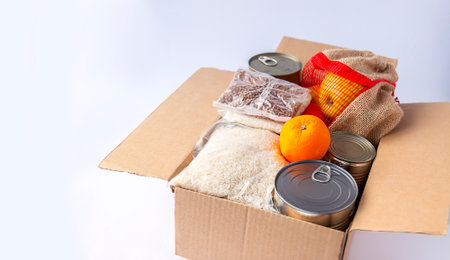 Tin cans, fresh apple fruits, buckwheat and rice packs in a cardboard box. Food donation, delivery theme.の写真素材