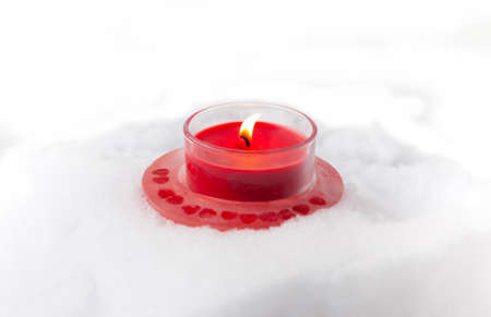 Burning red Christmas candle on fresh snow background.の写真素材