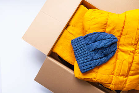 Warm yellow jacket and blue knitted cap in the opened cardboard box. Fashion outfit. Bright colors. Home storage. Small space organizing.の写真素材