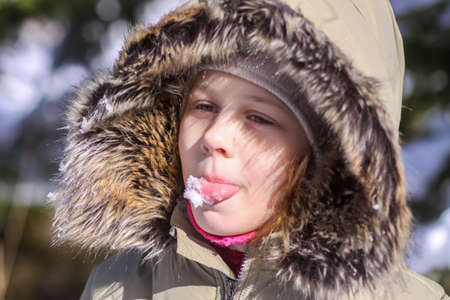 A little girl catching snowflakes on the tongue. Happy child walking outdoors in cold sunny day and...