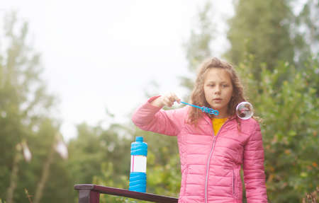 Funny little girl playing with soap bubbles on summer nature background.