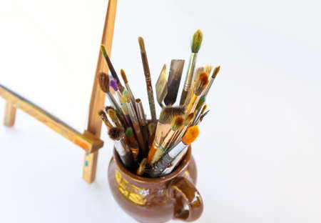 Artist's workplace. Canvas on the wooden easel and brushes in ceramic jug.の写真素材