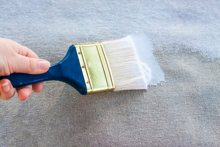 Synthetic paint brush and primer on canvas surface.
