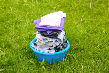 Colorful washed dry clothes in plastic bowl on the green grass background.の写真素材