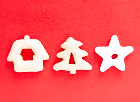 Christmas cookies shaped like a star, house, and tree on a red surface. A warm symbol of holiday spirit and home comfort.の写真素材