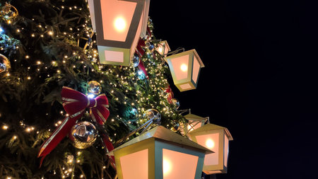 Twinkling lights and ornaments shine on a tree in a bustling urban setting. The image communicates...