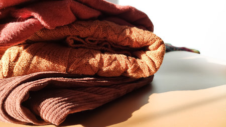Cozy sweaters are piled together under warm sunlight. The moment reflects softness, warmth, and peaceful everyday living.の写真素材