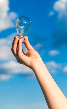 Hand Holding Brillant Bulb With Blue Sky Background の写真素材