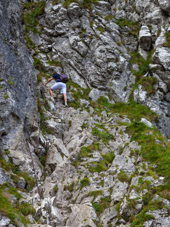 Man with backpack climbing a rock difficult and dangerous path using chains.のeditorial素材