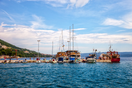 Tourists and locals walk the stone wharf against boats line the docks by the marina of Omis, Croatia.のeditorial素材
