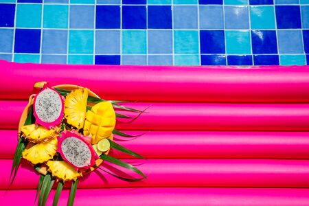 tropical fruits mango, dragon fruit, papaya and pineapple on a plate near an inflatable pink...