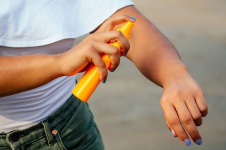 hands of a dark-skinned woman close up holding a bottle of sunscreen spray applying spf cream on...