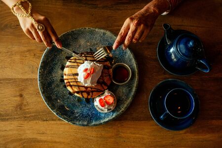 whipped cream,honey and strawberries on waffles pancakes on the table is a cup with tea and a teapot...