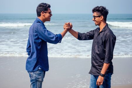 Happy holi two indian stylish mans young friends hugging on the beach by the sea.long-awaited meeting diwali of the brothers in India Goa tropical paradise summer vacation blue sky and oceanの写真素材
