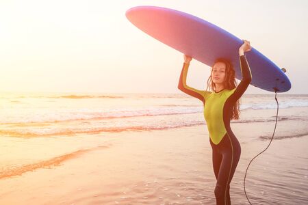Beautiful woman in a diving suit for swimming surfing in the Indian Ocean on the background sunset sky and waves.professional surfer girl in a wetsuit doing sports at sea.extreme, adrenaline and youthの写真素材