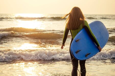 Beautiful woman in a diving suit for swimming surfing in the Indian Ocean on the background sunset...