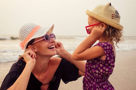 Young mother with little girl on her back at beach in summer. Happy family having fun summer vacationの写真素材