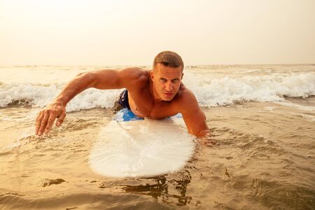 surfing freelancing man muscle and press sport training on the beach at sunset.male fitness model...