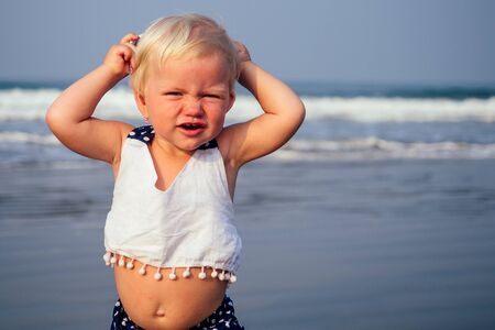 Adorable small sleepy girl at beach applying sunblock cream.one year old fair-haired baby child...